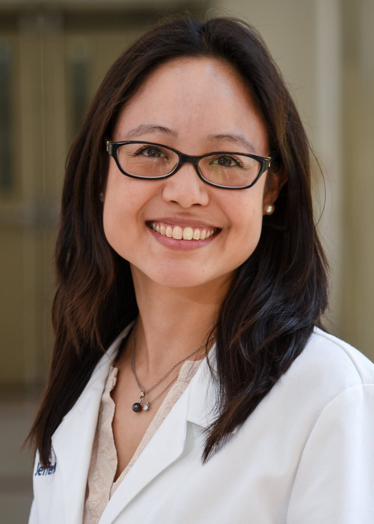 This image shows a headshot photo of Julie Barta smiling wearing glasses and a white lab coat.