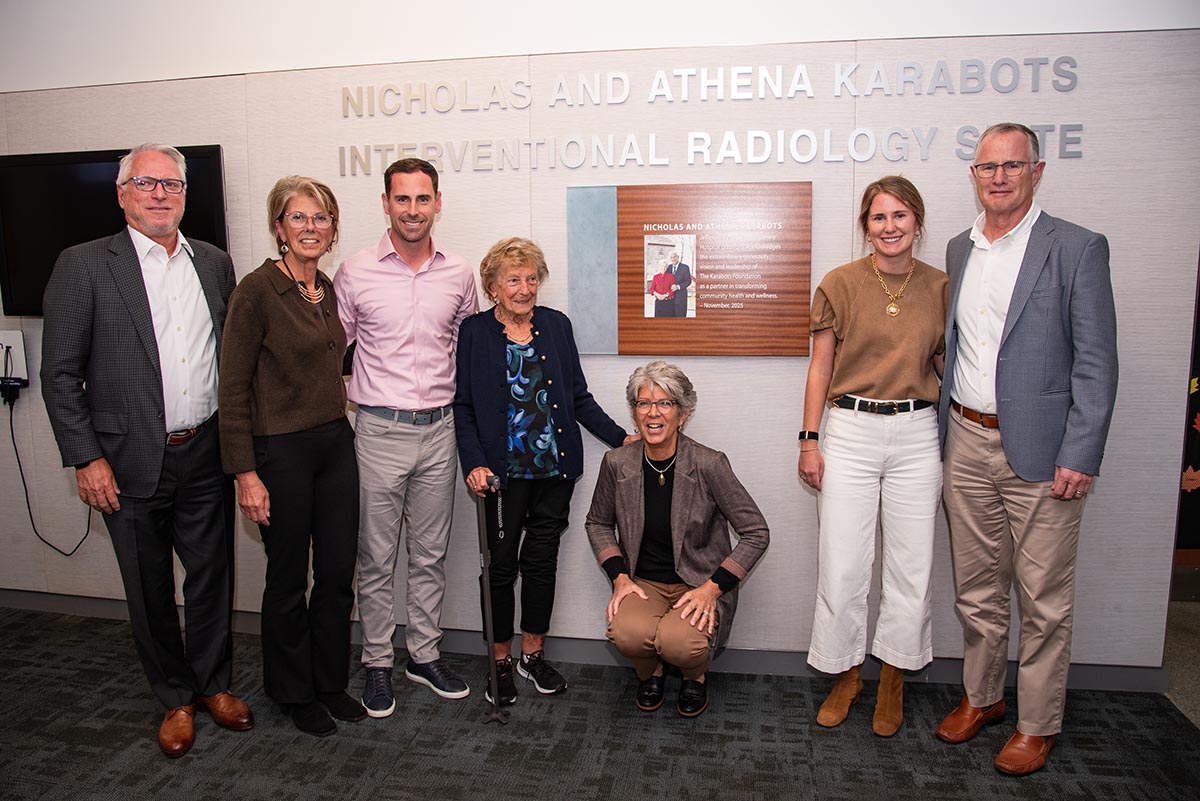 This image shows seven people posing for a photo in front of the new Nicholas and Athena Karabots Diagnostic Center and Interventional Radiology Suite.