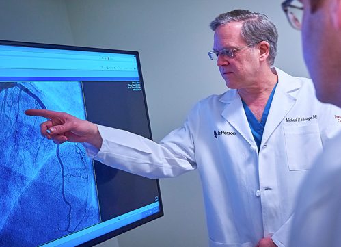 A doctor in a white lab coat points to heart imaging on a screen.