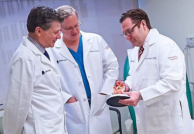 Three doctors in white lab coats look at a replica heart.