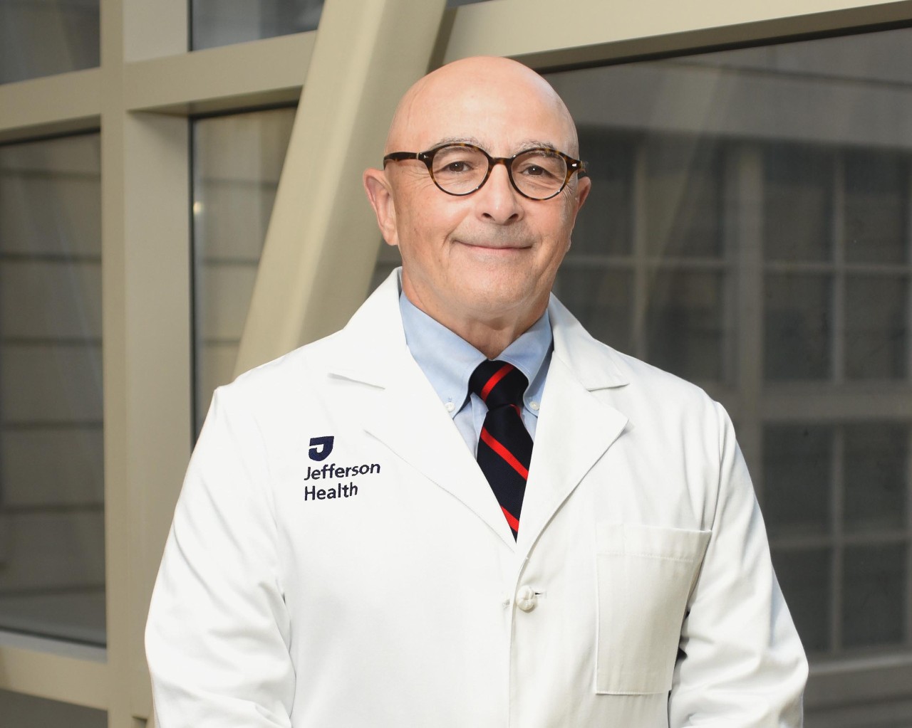 This image shows a photo of Geno J. Merli, MD, MACP, FHM, FSVM wearing a white lab coat.