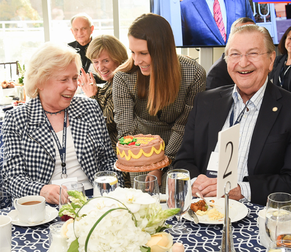This image shows Suzanne Springer Zeok, MD ’69, and John V. Zeok, MD ’67, smiling while being presented with a cake.
