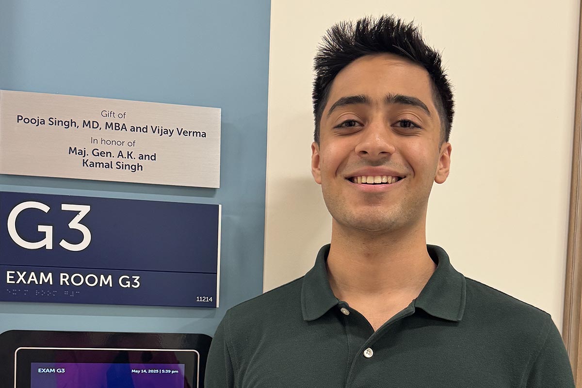 This image shows Dr. Pooja Singh's son in front of a plaque for the Honickman Center exam room dedicated to her father.