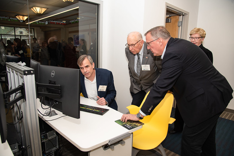 This image shows John Thackrah (center) and two others looking at one of the new Bloomberg terminal data feeds in the Thackrah Capital Markets Research Lab.